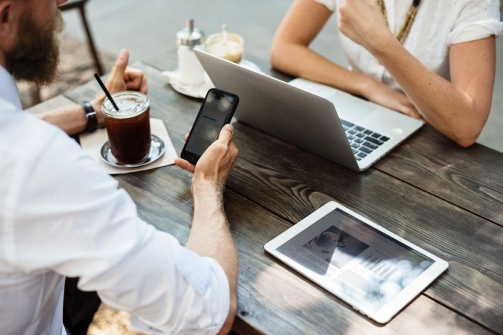 Zwei Geschäftsleute treffen sich in einem Café mit Laptop, Tablet und Mobiltelefon